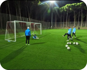 Goalkeeper training session on a floodlit artificial pitch at night with multiple players and balls