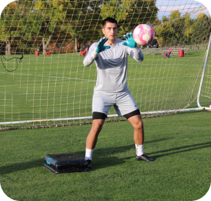 Goalkeeper in black kit in a low ready stance during solo training on an artificial turf field
