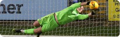 Goalkeeper in green kit making a full-stretch diving save during a night match