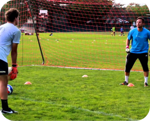 Two goalkeepers in blue shirts training together in front of a goal with cones on the grass
