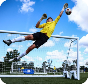 Goalkeeper in yellow kit making a diving fingertip save against a blue sky