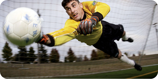 Goalkeeper in yellow kit making a dramatic full-stretch diving save outdoors